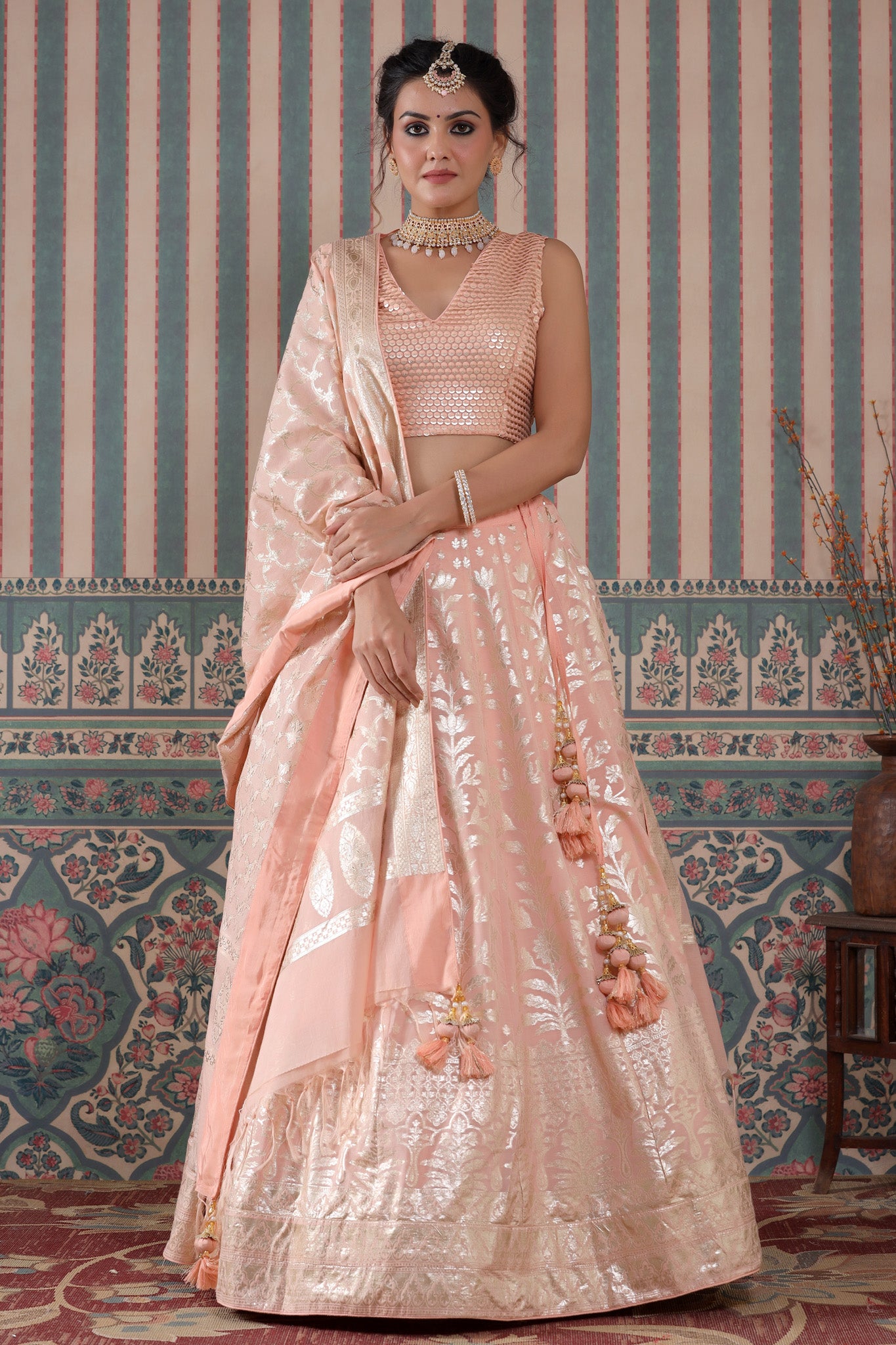 Shop a peach lehenga set featuring a floral zari embroidered silk lehenga set. It comes with a beautiful V-neck blouse and zip closure. It has tassels attached to the lehenga. Pair it with beautiful jewelry to enhance your look. Shop online from Pure Elegance.