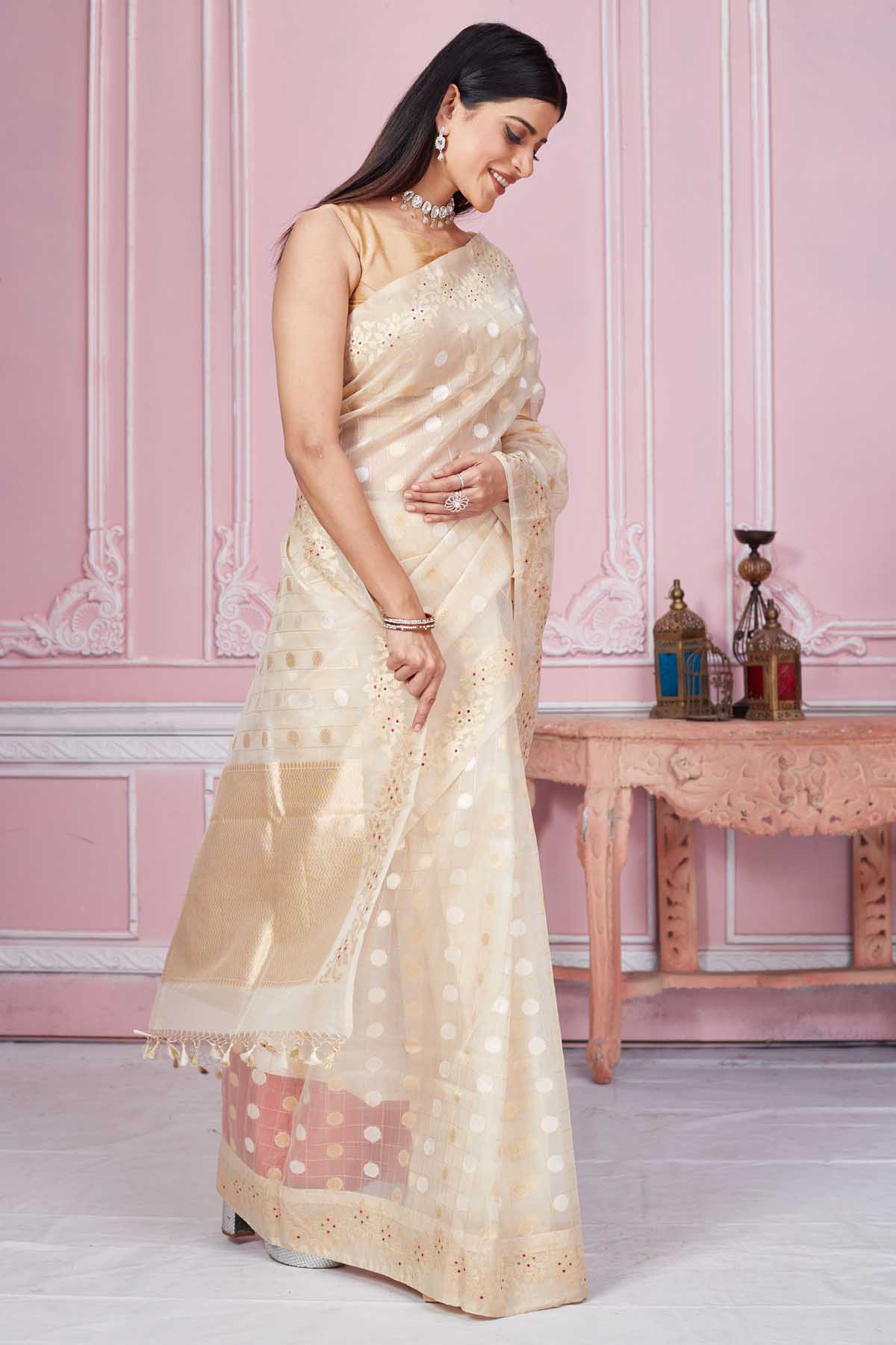 Shop cream Banarasi saree online in USA with scattered buti and zari border. Look your best on festive occasions in latest designer saris, pure silk sarees, Kanjivaram silk sarees, handwoven saris, tussar silk sarees, embroidered saris from Pure Elegance Indian fashion store in USA.-side