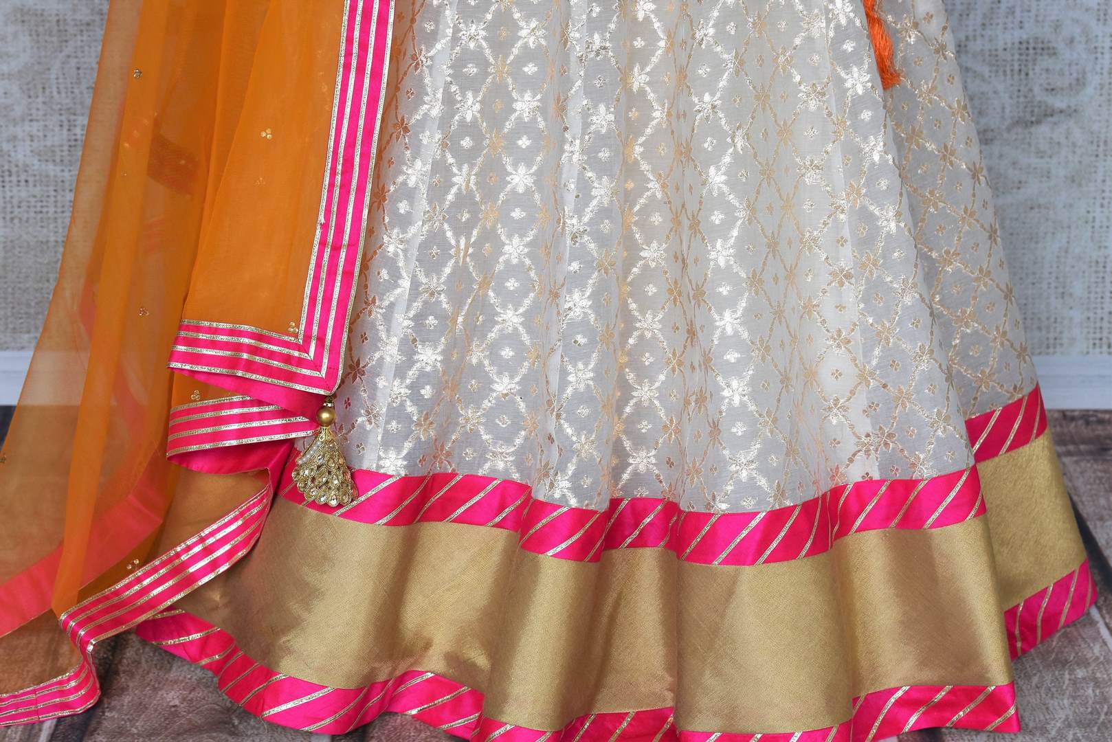 Leave them spellbound as you show up in this jaw-dropping white chanderi silk lehenga accompanied with a stunning hot pink zardosi embroidered blouse. Complete the look with the orange sequinned net dupatta with pink border. Shop Indian dress, lehenga choli, ikkat sari online or visit Pure Elegance store, USA.-lehenga