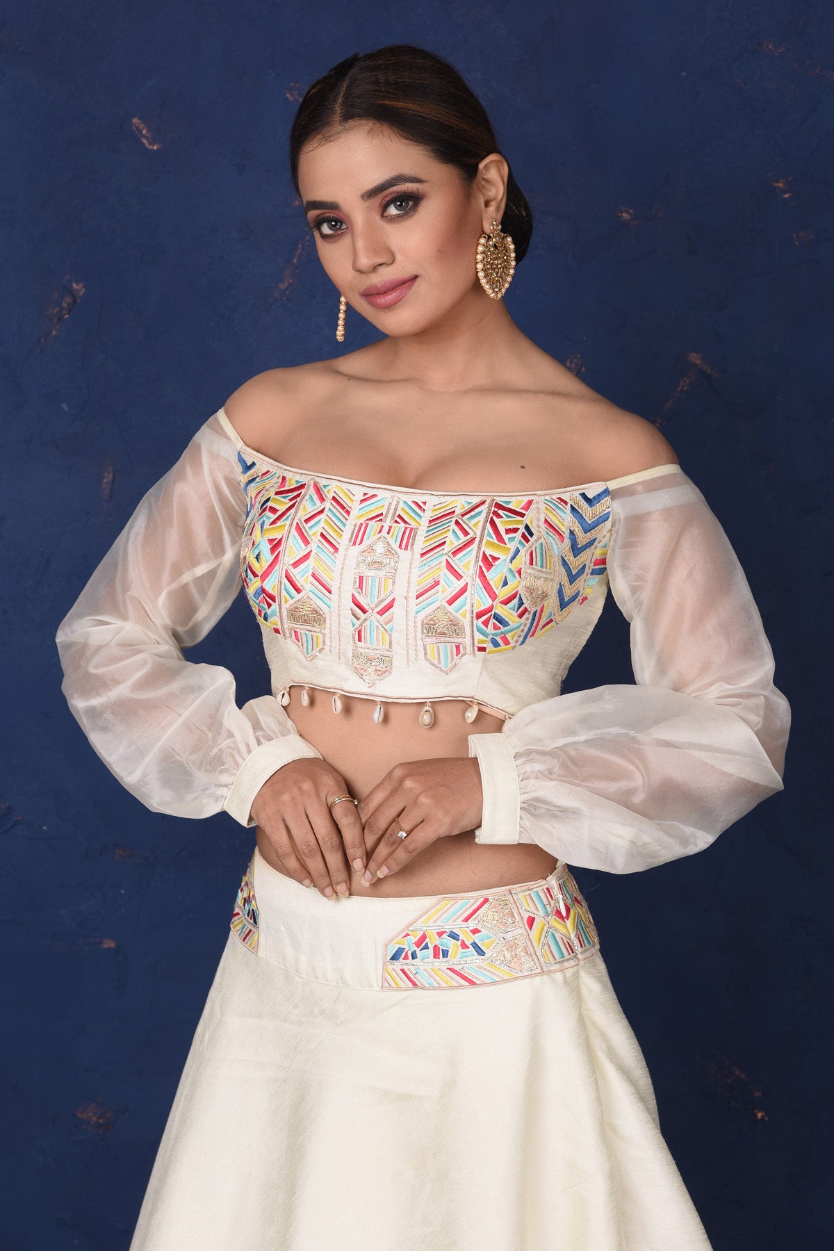 Shop elegant cream embroidered off-shoulder designer lehenga online in USA with dupatta. Set fashion goals on special occasions in exclusive designer lehengas, Indian suits, Anarkali dresses, designer gowns, bridal lehengas from Pure Elegance Indian fashion store in USA.-closeup
