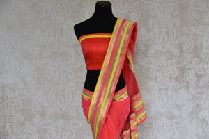 90A492 Coral red sari from India with multi-colored border & designer blouse. Buy this net saree, perfect for party wear, online at our Indian clothing store - Pure Elegance and get set to wow.