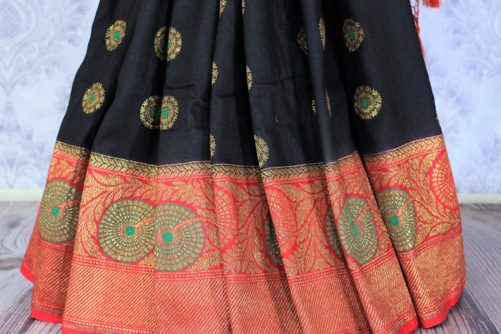 This black buta work muga banarsi silk sari complemented with a stunning red zari border and a heavily embroidered woven red pallu adds a touch of grace. Style it with a red designer blouse to strut at weddings or parties. Shop designer silk sarees, printed saris online or visit Pure Elegance store, USA. -pleats