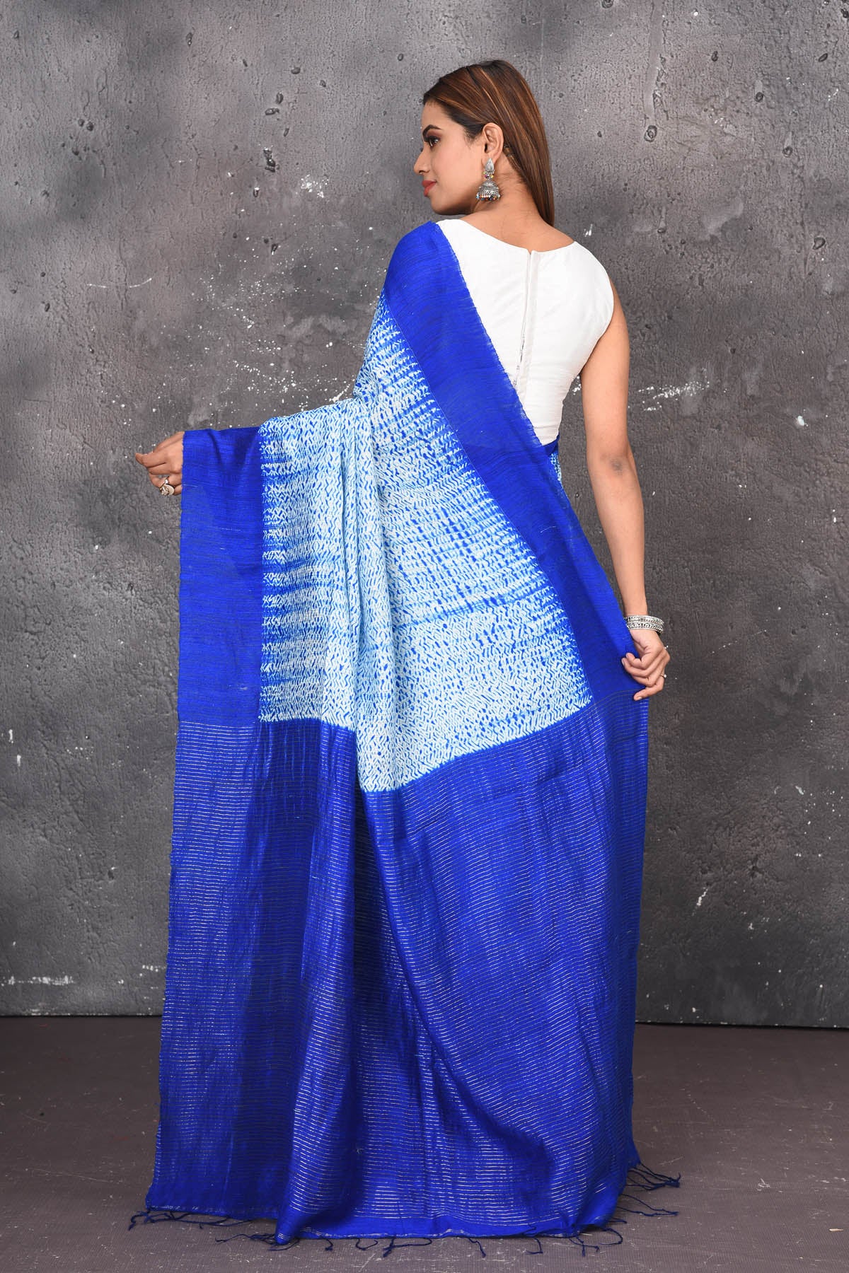 Shop this elegant offwhite-blue handloom shibori tussar saree online in USA which is handcrafted from fine silk tussar fabric, this tie and dye saree brings out the nature of flow. You can pair this beautiful shibori print with minimal jewellery for a casual day outfit. Add this plain shibori saree to your collection from Pure Elegance Indian fashion store in USA.-Back view with open pallu.