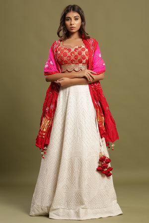 Shop White self-embroidered Zari lehenga set featuring bandhej dual print dupatta and zari & gota patti embroidered red blouse. The lehenga also has a long tassel attached to tie the knot. Pair it with beautiful jewelry to enhance your look. Shop online from Pure Elegance.