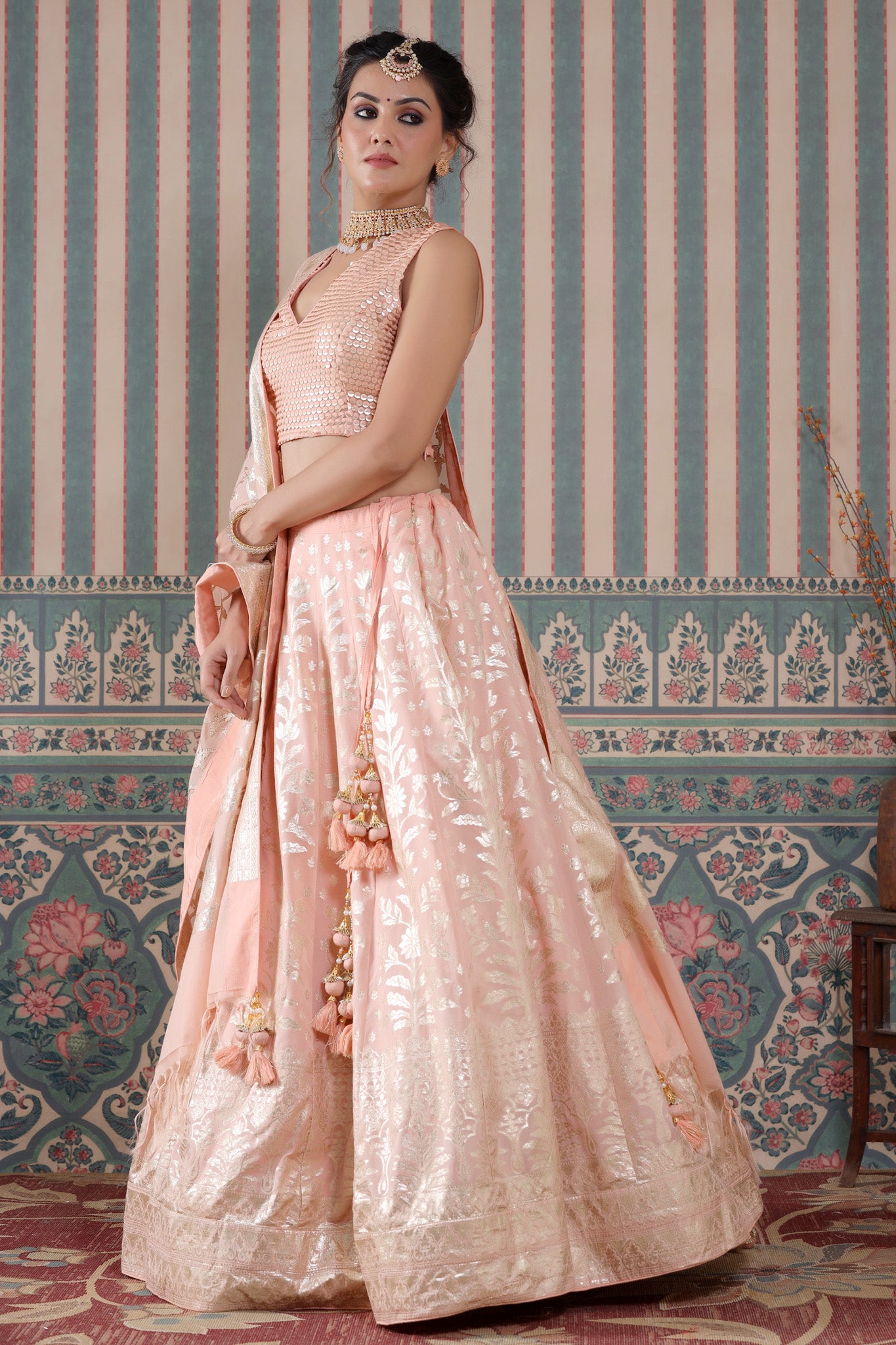 Shop a peach lehenga set featuring a floral zari embroidered silk lehenga set. It comes with a beautiful V-neck blouse and zip closure. It has tassels attached to the lehenga. Pair it with beautiful jewelry to enhance your look. Shop online from Pure Elegance.