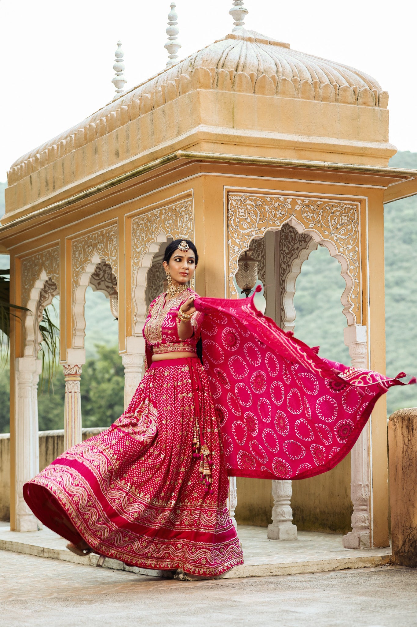 Shop a Pink bandhej print beautiful lehenga set with gota patti work and a long tassel attached to the lehenga. it comes with a pink blouse with front embroidery, hook closure, and tie-up at the back. Pair it with beautiful Rajasthani jewelry to enhance your look. Shop online from Pure Elegance.