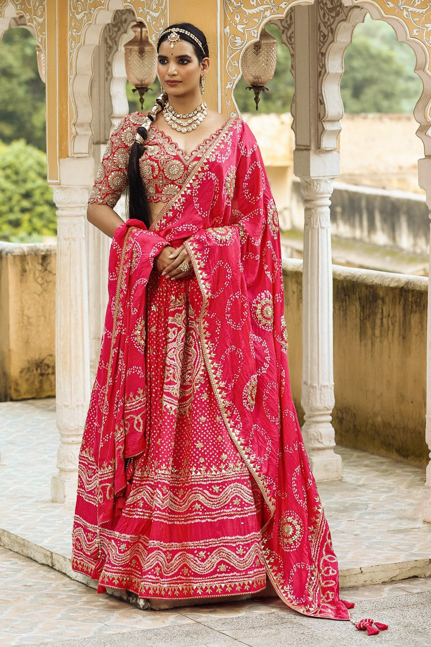 Shop a pink bandhej print beautiful lehenga set with gota patti work and long tassel attached on the lehenga. it comes with a pink blouse with heavy embroidery, hook closure, and tie-up at the back. Pair it with beautiful Rajasthani jewelry to enhance your look. Shop online from Pure Elegance.