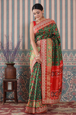Shop green Patola silk sari online in USA with red embroidered border. Make a fashion statement at weddings with stunning designer sarees, embroidered sarees with blouse, wedding sarees, handloom sarees from Pure Elegance Indian fashion store in USA.-front
