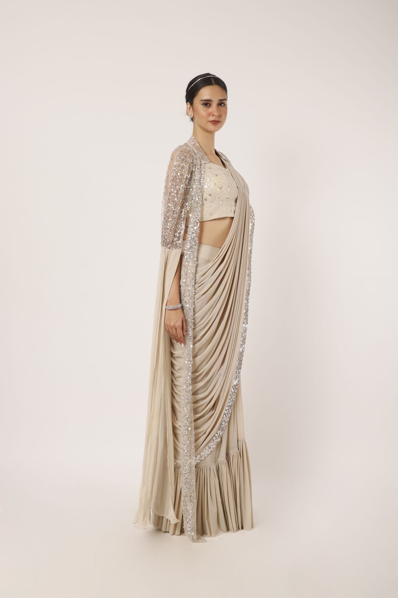 Shop a beige drape saree with statement cape sleeves. Make a fashion statement on festive occasions and weddings with designer sarees, designer suits, Indian dresses, Anarkali suits, palazzo suits, designer gowns, sharara suits, and embroidered sarees from Pure Elegance Indian fashion store in the USA.