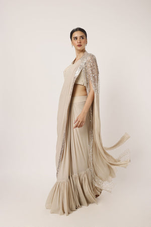Shop a beige drape saree with statement cape sleeves. Make a fashion statement on festive occasions and weddings with designer sarees, designer suits, Indian dresses, Anarkali suits, palazzo suits, designer gowns, sharara suits, and embroidered sarees from Pure Elegance Indian fashion store in the USA.