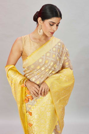 Shop cream Kora Banarasi sari online in USA with heavy yellow border. Look your best on festive occasions in latest designer sarees, pure silk sarees, Kanjivaram silk saris, handwoven saris, tussar silk sarees, embroidered saris from Pure Elegance Indian clothing store in USA.-closeup