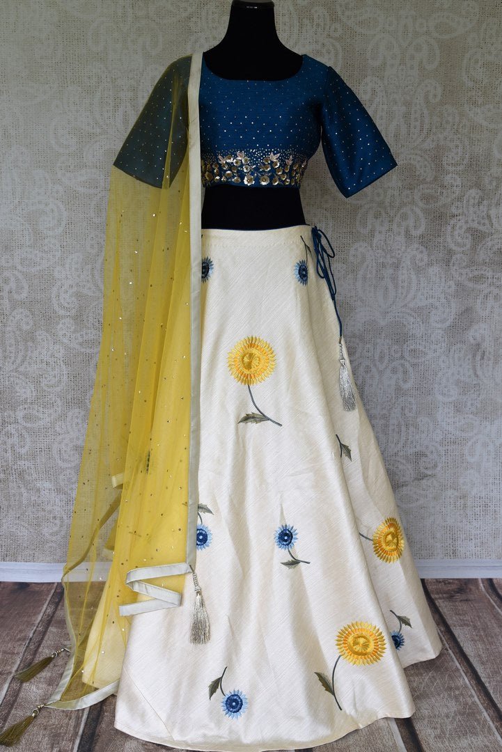 Be the kitchsy conversation-starter in this white floral embroidered raw silk lehenga. It comes with a royal blue silk blouse with intricate embroidery. Drape a yellow sequin work dupatta for an easy breezy chic look. Shop handcrafted lehenga choli, anarkali suits, saris online or visit Pure Elegance store, USA. -full view