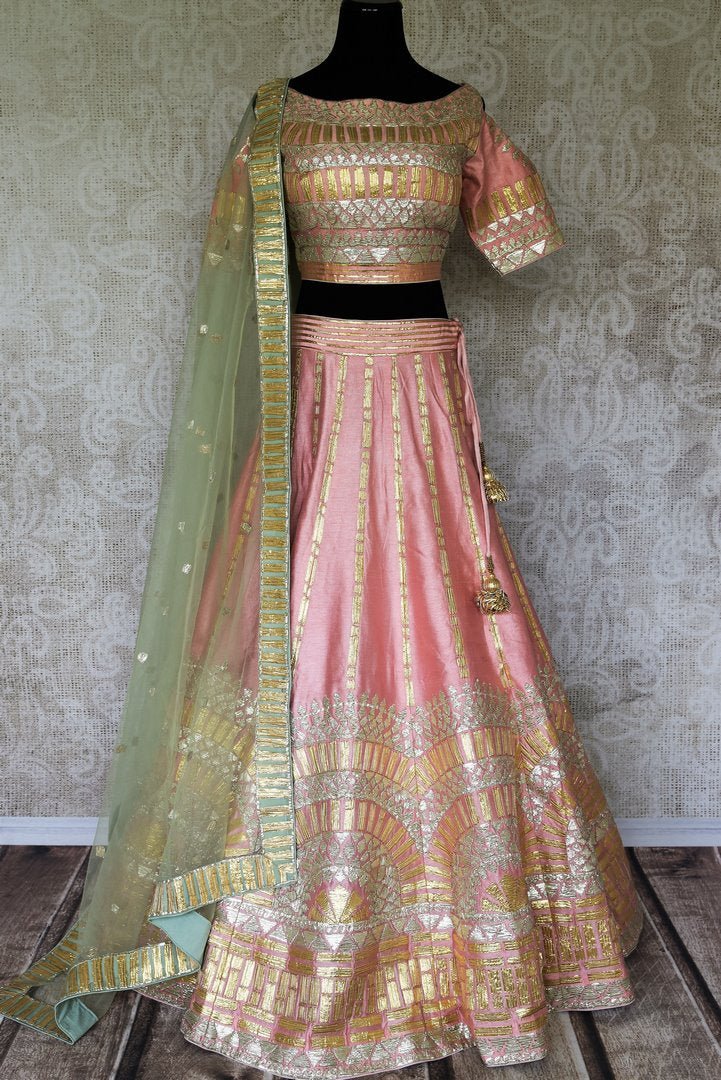 Embrace the pastel drama in this stunning soft pink raw silk lehenga with intricate gota work. It comes with a matching pink gota work raw silk cold shoulder blouse and a beige gota work dupatta. Shop authentic silk sarees, anarkali suits, dress online or visit Pure Elegance store, USA. -full view