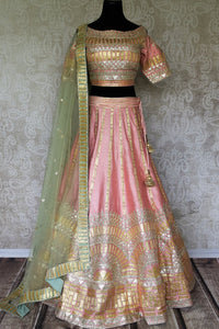 Embrace the pastel drama in this stunning soft pink raw silk lehenga with intricate gota work. It comes with a matching pink gota work raw silk cold shoulder blouse and a beige gota work dupatta. Shop authentic silk sarees, anarkali suits, dress online or visit Pure Elegance store, USA. -full view