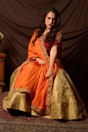 Buy gorgeous maroon and green embroidered brocade lehenga online in USA with orange dupatta. Shine at weddings and special occasions with beautiful Indian designer dresses, gowns, lehengas from Pure Elegance Indian clothing store in USA.-sitting