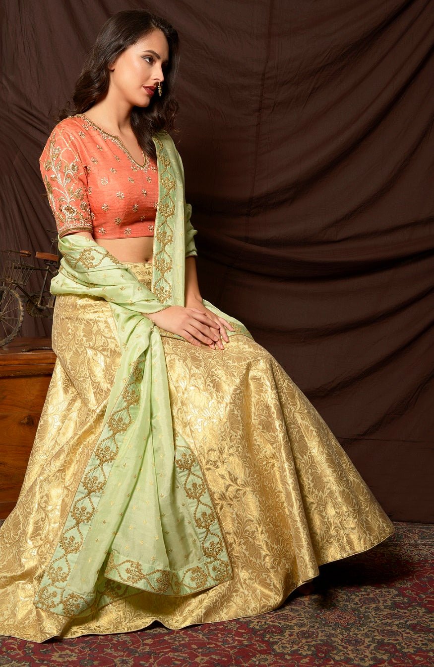 Shop gorgeous peach and gold embroidered brocade lehenga online in USA with pista green dupatta. Shine at weddings and special occasions with beautiful Indian designer dresses, gowns, lehengas from Pure Elegance Indian clothing store in USA.-sitting