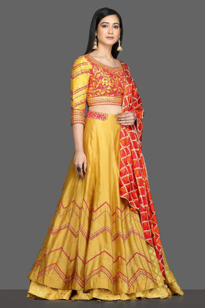 Buy gorgeous yellow embroidered lehenga online in USA with red and orange dupatta. Dazzle on weddings and special occasions with exquisite Indian designer dresses, sharara suits, Anarkali suits, bridal lehegas from Pure Elegance Indian fashion store in USA.-side