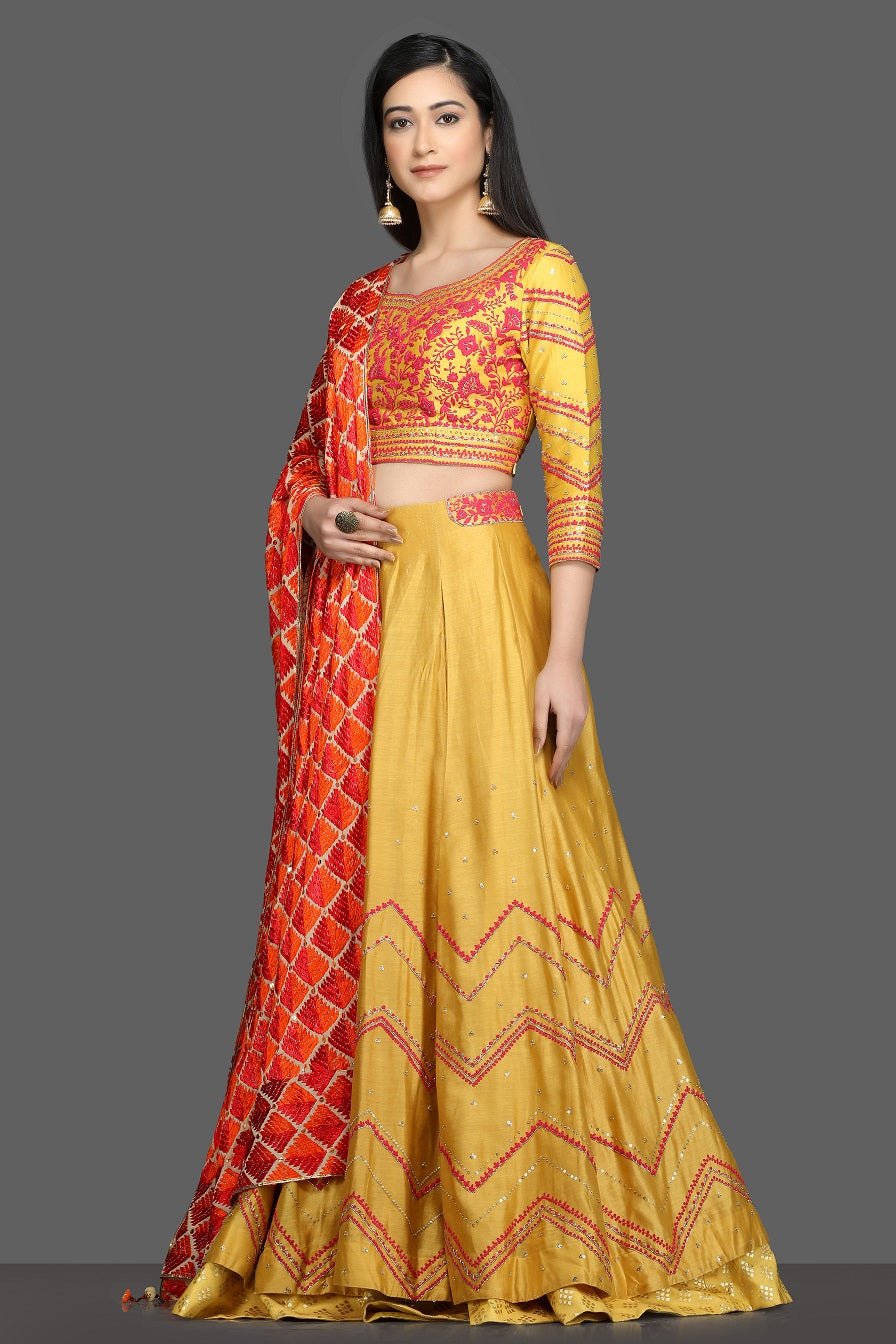 Buy gorgeous yellow embroidered lehenga online in USA with red and orange dupatta. Dazzle on weddings and special occasions with exquisite Indian designer dresses, sharara suits, Anarkali suits, bridal lehegas from Pure Elegance Indian fashion store in USA.-left