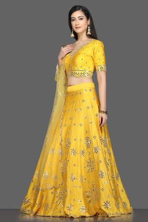 Shop gorgeous bright yellow mirror work lehenga online in USA with net dupatta. Dazzle on weddings and special occasions with exquisite Indian designer dresses, sharara suits, Anarkali suits, bridal lehegas from Pure Elegance Indian fashion store in USA.-left
