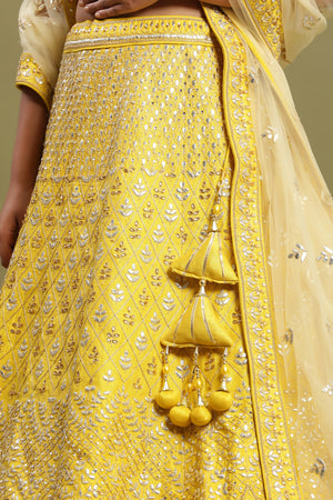 Shop a Beautiful yellow silk lehenga with a net dupatta. The lehenga is perfect for weddings and sangeet parties. It is crafted in silk with intrinsic golden silver gotta patti work and a beautiful off-white blouse. Shop online from Pure Elegance.