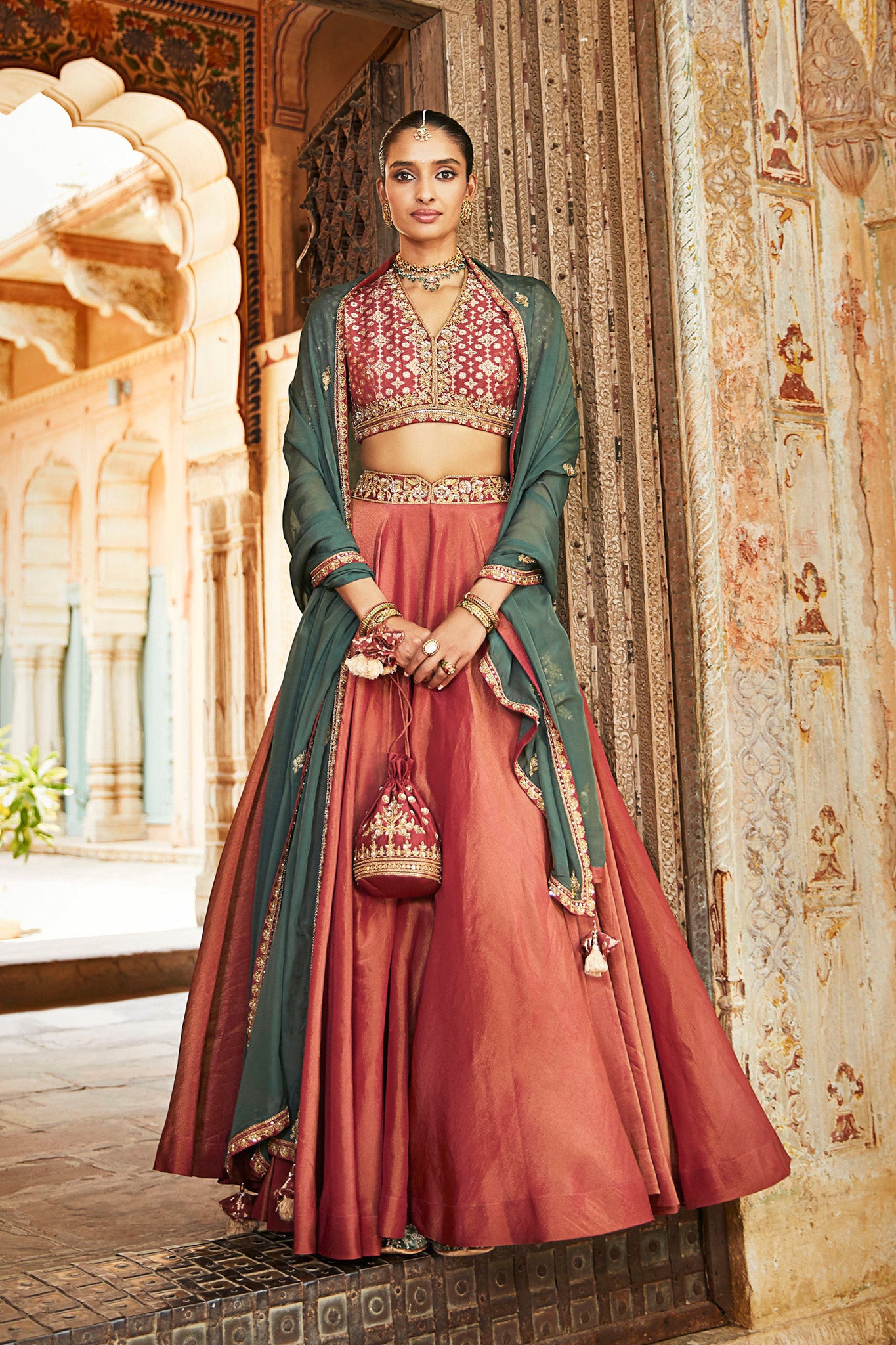 Gorgeous rust color embroidered tissue lehenga with dupatta is a perfect choice for a sangeet and engagement parties. The lehenga is adorned with beautiful embroidery and a contrasting dupatta. Shop designer Indian lehengas in USA from Pure Elegance.- Front View