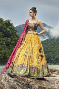 Shop this beautiful yellow lehenga with purple choli and pink georgette dupatta. The lehenga is perfect for haldi and sangeet parties. Shop online from Pure Elegance.