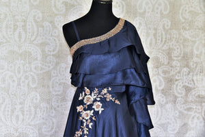 Step down the aisle in our designer royal blue one-shoulder dress. This gorgeous floral embroidered dress with ruffled crest comes with a gold hand woven neckline that further accentuates the beauty of this ensemble. Shop Indian dresses, anarkali suits and lehenga sets online or visit Pure Elegance store, USA. -front view