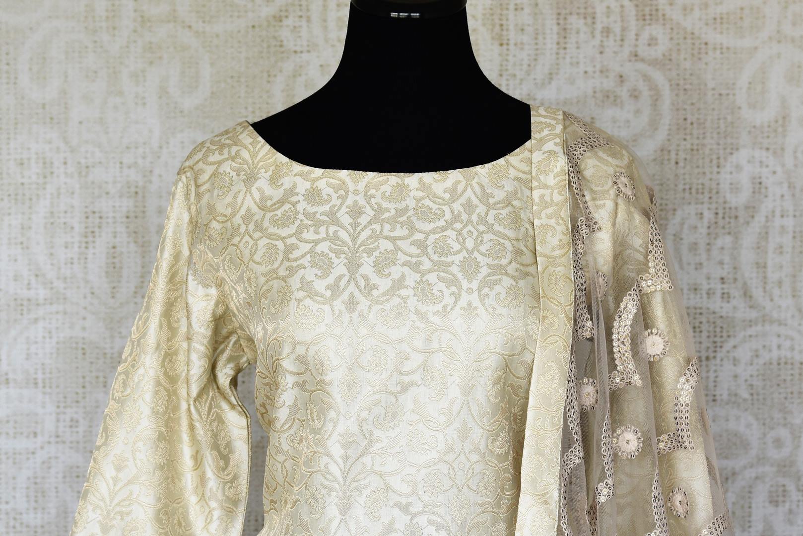 Shop cream embroidered Banarasi silk suit online in USA with grey silk sharara. Keep your wardrobe update with latest Indian clothing from Pure Elegance Indian fashion store in USA. Shop beautiful Indian designer lehengas, Anarkali suits, gowns for Indian women in USA from our online store.-front