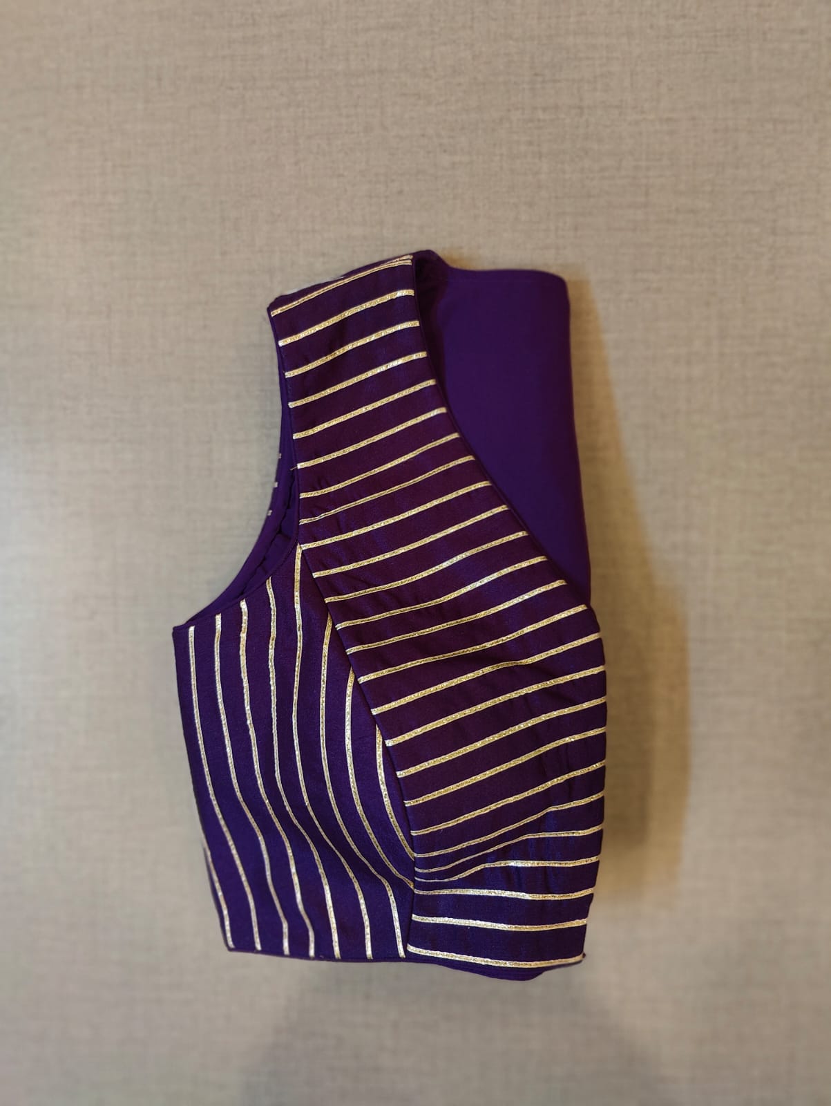 Buy Festive essentials and get an elevated twist with this purple-striped blouse. Featuring a golden strip, the blouse is cut with, V-neck, and is sleeveless. Wear it with a contrasting saree or even with a contrasting lehenga skirt to complete the look. Elevate your Indian saree style with exquisite readymade sari blouses, embroidered saree blouses, Banarasi sari blouses, and designer sari blouse from Pure Elegance Indian clothing store in the USA.- Folded View