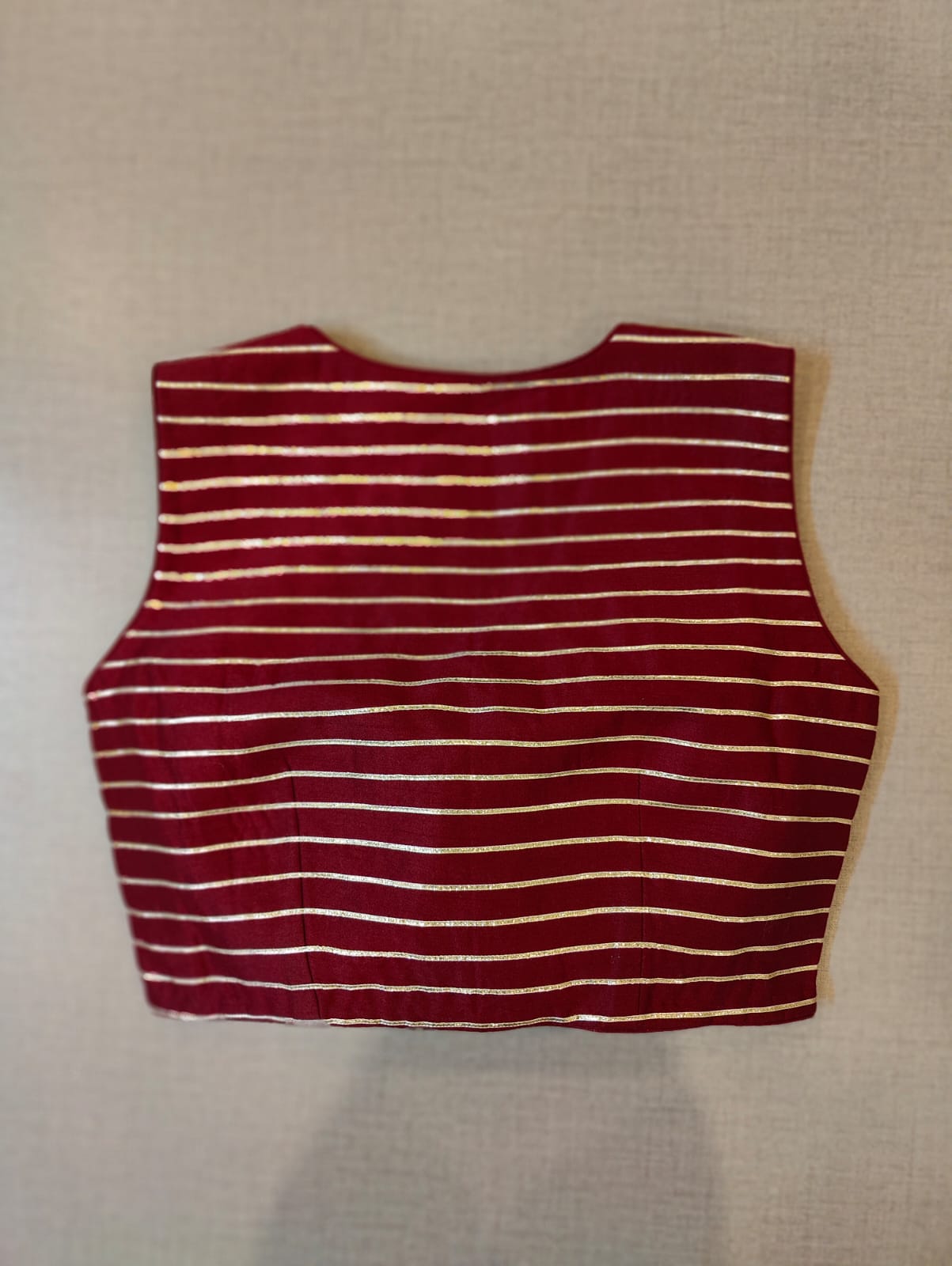 Buy Festive essentials and get an elevated twist with this maroon-striped blouse. Featuring a golden strip, the blouse is cut with, V-neck, and is sleeveless. Wear it with a contrasting saree or even with a contrasting lehenga skirt to complete the look. Elevate your Indian saree style with exquisite readymade sari blouses, embroidered saree blouses, Banarasi sari blouses, and designer sari blouses from Pure Elegance Indian clothing store in the USA.- Back View
