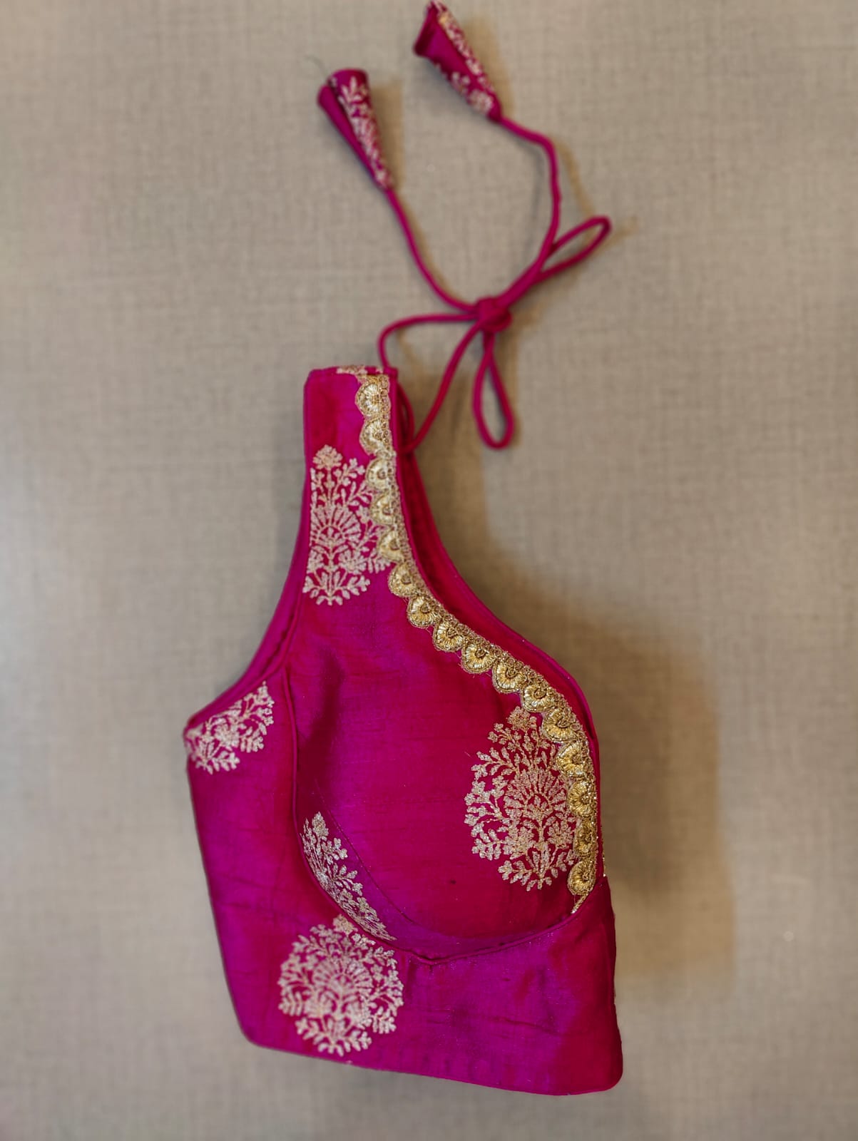 Buy minimal yet stylish, this pink blouse with golden patches and neck embroidery will brighten up your festive soirees. Featuring the blouse is V-neck in front and U shape in the back, and sleeveless with hook closure and tie up. Wear it with a contrasting saree or even with a contrasting lehenga skirt to complete the look.- Folded View