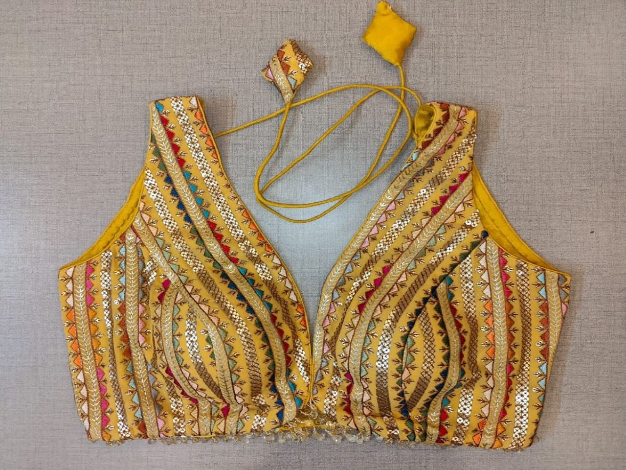 Buy a yellow-golden gotta Patti embroidery saree blouse that has a V-neck, is sleeveless, has a hook, and has a tie-up closure at the back. Drape a saree over this pretty blouse and be the start of any function. You can also style it with a palazzo to create a fusion outfit.  Elevate your Indian saree style with exquisite readymade sari blouses, embroidered saree blouses, Banarasi sari blouses, and designer sari blouses from Pure Elegance Indian clothing store in the USA.- Front View