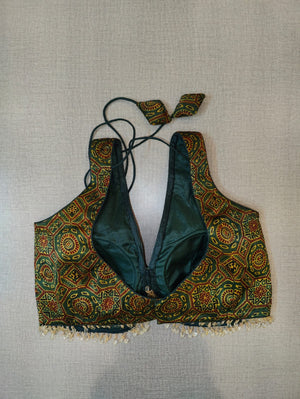 Buy a green block printed padded saree blouse, that has a V-neck, short sleeves, tie-up detail at the back, hook, and eye closure. Let your aura shine throughout by wearing this designer saree blouse. Pair this fashionable blouse with a beautiful printed sari and statement neck piece and you are good to go. - Back View