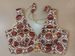 Buy a white block printed padded saree blouse, that has a V-neck, short sleeves, tie-up detail at the back, hook, and eye closure. Let your aura shine throughout by wearing this designer saree blouse. Pair this fashionable blouse with a beautiful printed sari and statement neck piece and you are good to go.- Front View
