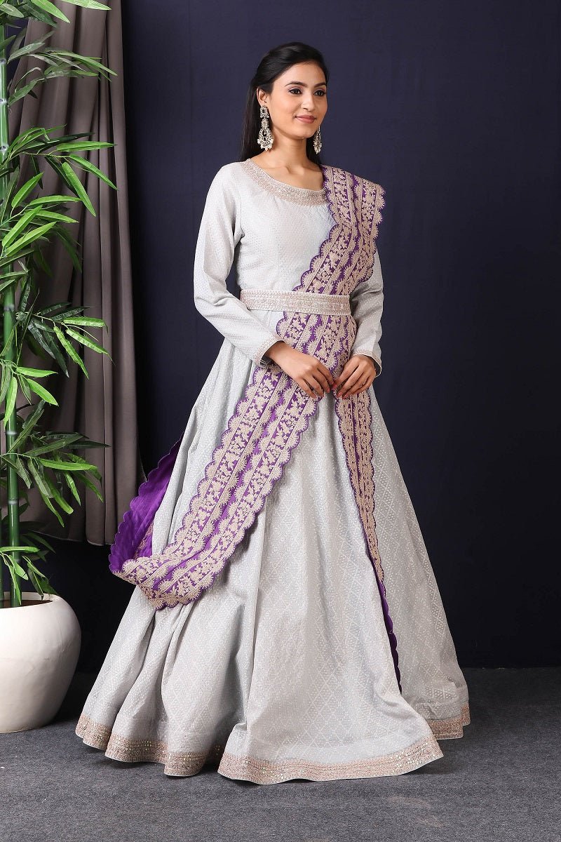 Shop this designer Indo western Anarkali in grey and purple color. This anarkali comes in chanderi silk fabric which has zari dori work around neck and maharani belt with embroidery work. The borders of this anarkali have an exquisite design that is eye-catchy and has lace work on it. Buy designer anarkali attire from Pure Elegance Indian saree store in USA.-Side view.