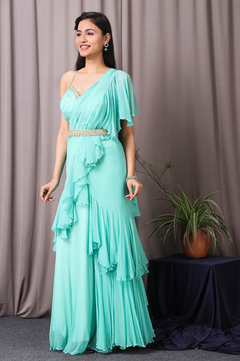 Shop this designer indo western Saree in aqua blue colour. This saree comes in chiffon and upadda silk fabric. The borders of the saree have an exquisite design that is eye-catchy and has sequin and thread embroidery work on it. Complete the look with embroidered blouse showcasing floral and animal motifs especially around the neckline and on the backside. Shop this designer from Pure Elegance Online Indian store now.-Side view.
