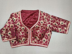 Buy this maroon and gold-colored brocade is woven design padded saree blouse that has a round neck, short sleeves, front opening with hook, and eye closure. Pair this fashionable blouse with a beautiful solid sari and statement neckpiece and you are good to go! Buy this designer blouse in the USA from Pure Elegance. -Front View