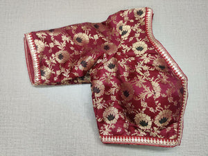 Buy this maroon and gold-colored brocade is woven design padded saree blouse that has a round neck, short sleeves, front opening with hook, and eye closure. Pair this fashionable blouse with a beautiful solid sari and statement neckpiece and you are good to go! Buy this designer blouse in the USA from Pure Elegance. -Folded View