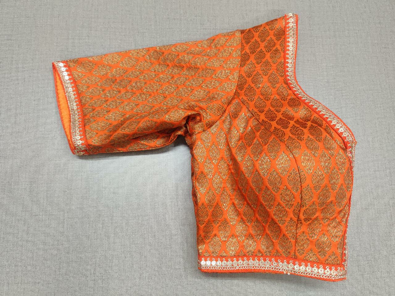 Orange and gold-colored solid saree padded blouse has a round neck, short sleeves, front closures, and hook-and-eye placket on the front . This blouse is great to buy. Pair this fashionable blouse with beautiful silk sarees and a statement neckpiece and you're good to go! Buy this designer blouse in USA from Pure Elegance. -Folded View