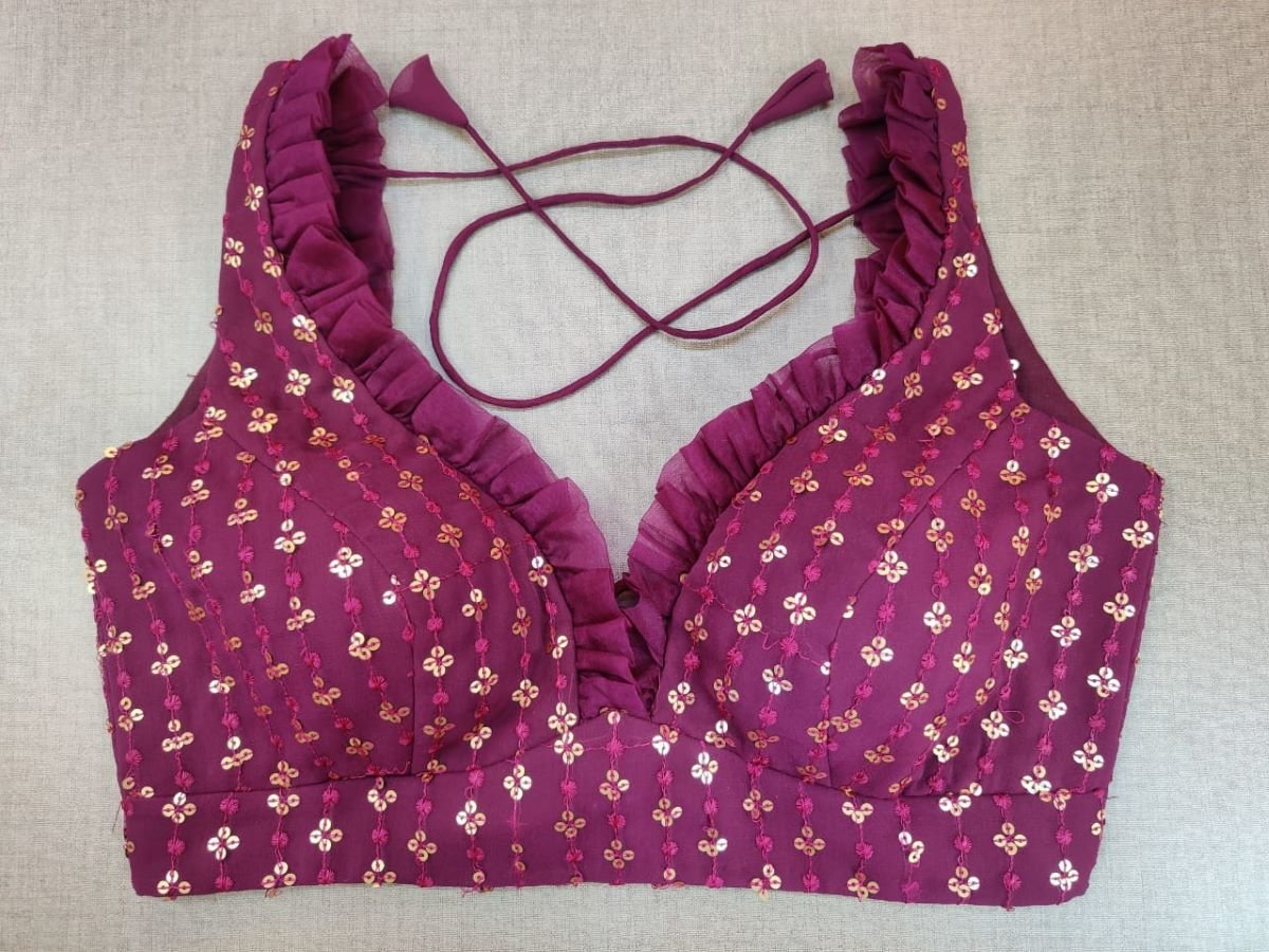 Buy a tap into the festive mood with this maroon blouse that is spruced up with gleaming details. Tailored in silk with a strappy neck, the blouse is adorned with golden embroidery work and frills on the neck in the front and back making the blouse more elegant. Buy this designer blouse in the USA from Pure Elegance. - Front View
