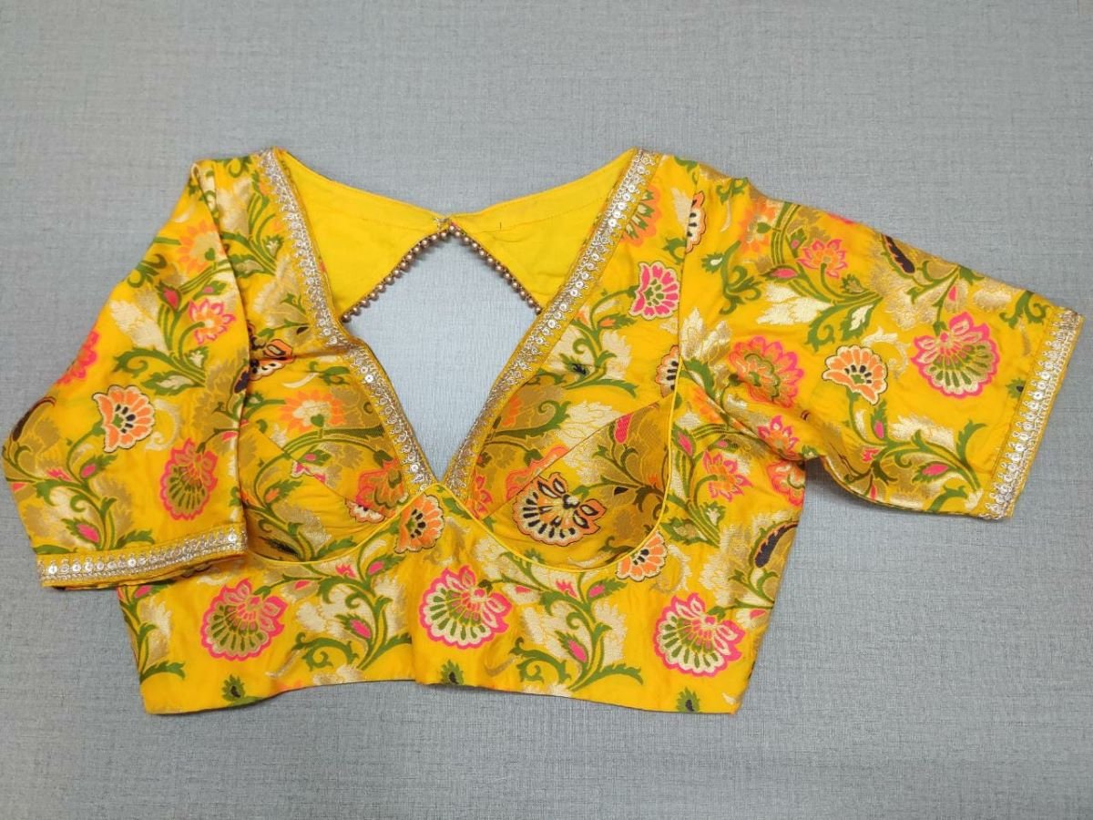 Buy a beautiful yellow color Indian saree designer blouse with floral print. You can pair up with any Indian Saree for any occasion to make your look elegant. A yellow multicolor floral blouse is a woven design padded saree blouse that has a V neck,  a beautiful back, and hook closure. You can pair it with any Indian Saree, Banarasi Silk Sarees, and Chanderi Silk sarees. Buy it from Pure Elegance sari blouse from Pure Elegance Indian clothing store in the USA.- Front View