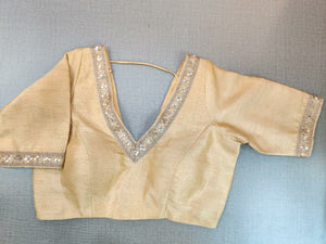 Buy a beautiful beige color Indian saree designer blouse with embroidery. You can pair up with any Indian Saree for any occasion to make your look elegant. A beige blouse is a woven design padded saree blouse that has a V neck,  a beautiful back, and hook closure. You can pair it with any Indian Saree, Banarasi Silk Sarees, and Chanderi Silk sarees. Buy it from Pure Elegance sari blouse from Pure Elegance Indian clothing store in the USA.- Front View