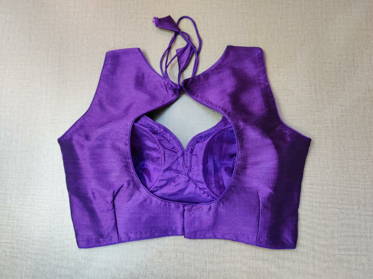 Buy a Purple readymade saree blouse that has sleeveless, a V-neck, hook-and-eye closure on the back, and tie-up detail on the back. This readymade saree blouse is a must-have piece. Wear it with a contrasting saree or even with a contrasting lehenga skirt to complete the look.- Back View