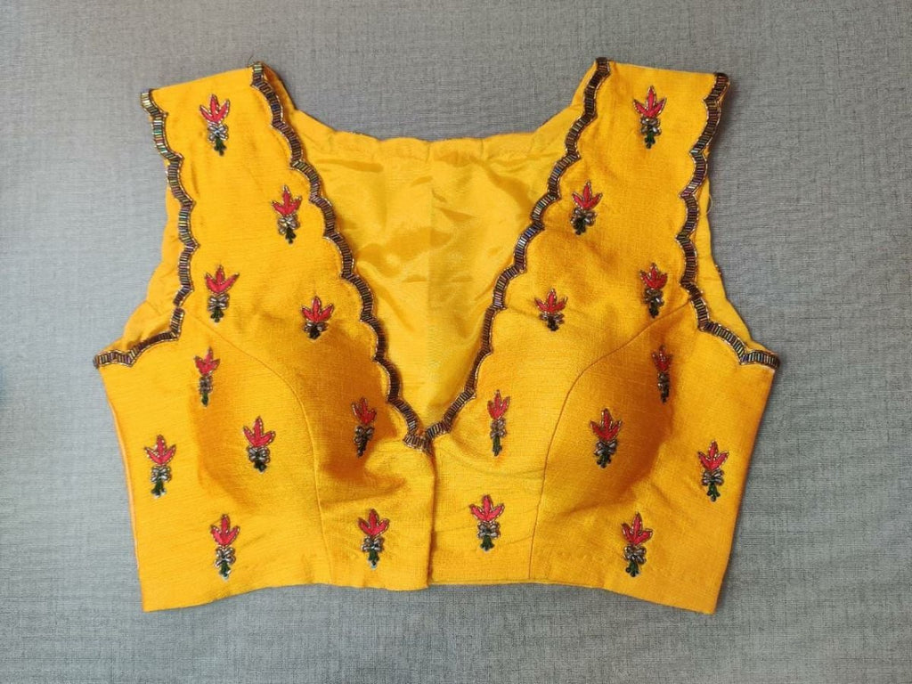 Buy this festive essential and get an elevated twist with this yellow floral embroidered blouse. Featuring an embroidered front & back, the blouse is cut with a tulip hem, V-neck, and sleeveless. Wear it with a contrasting saree or even with a contrasting lehenga skirt to complete the look.- Front View