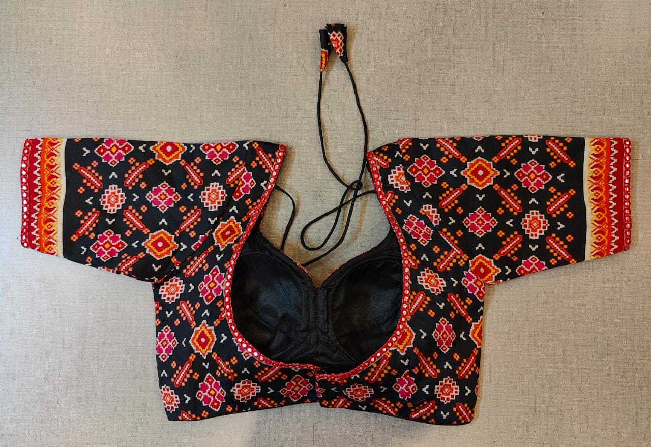 Buy this Black and Orange Block Printed, padded saree Blouse that has Short Sleeves, U neck with mirror work lace, hook, and tie-up closure, Pair it with a beautifully printed sari and statement neck piece and you are good to go! Elevate your Indian saree style with exquisite readymade sari blouses, embroidered saree blouses, Banarasi sari blouses, and designer sari blouses from Pure Elegance Indian clothing store in the USA.- Back View