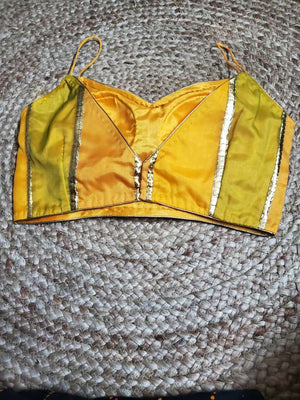Buy a yellow and green-colored silk saree blouse, padded, sleeveless, styled back, hook, and eye closure. This saree blouse is ought to grab the crowd's attention if you wear it with any banarasi saree. Glam up the ethnic look with high heels. Elevate your Indian saree style with exquisite readymade sari blouse, embroidered saree blouses, Banarasi sari blouse, and designer sari blouse from Pure Elegance Indian clothing store in USA.-Back View