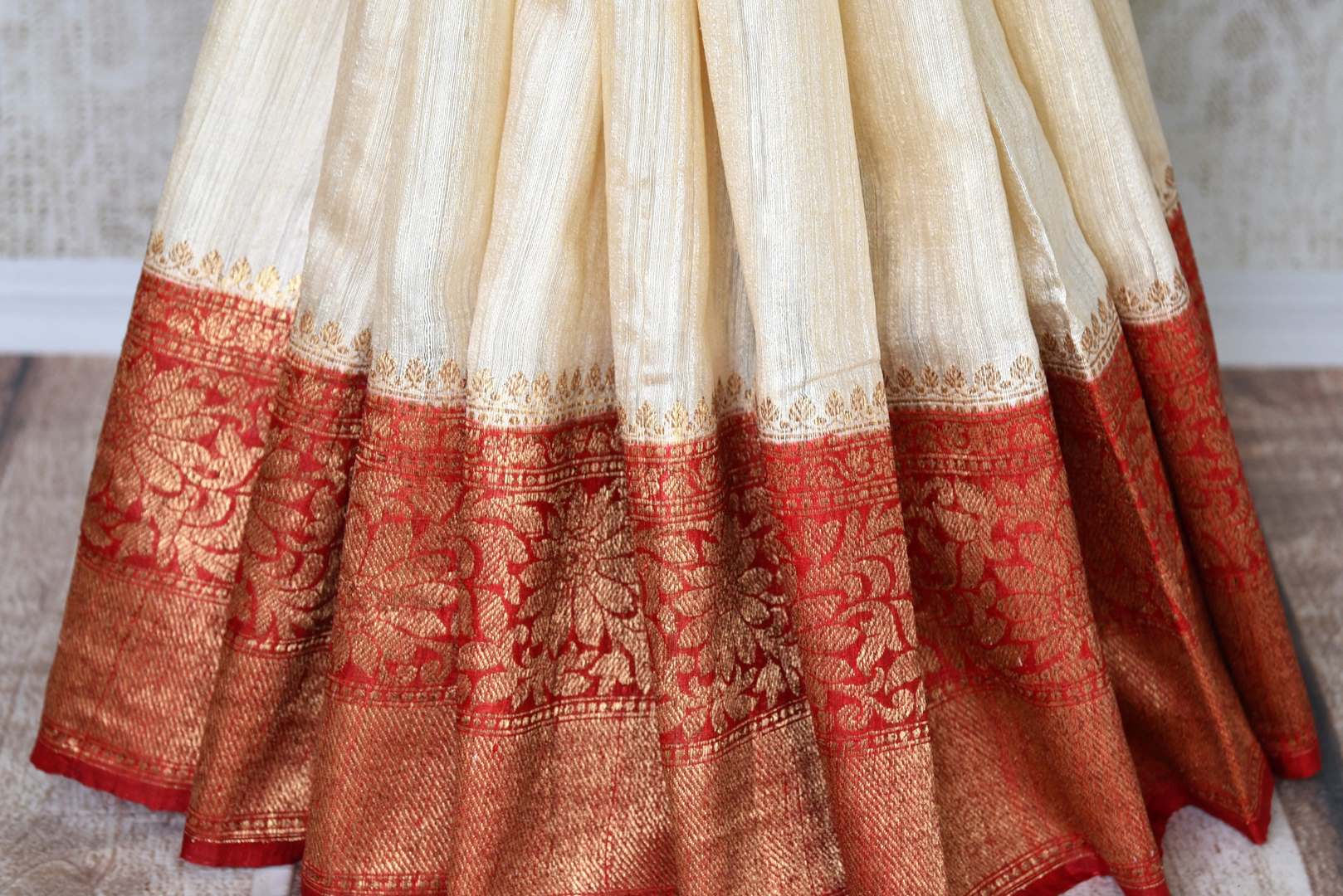 Fall in love with all things classic like this cream matka banarsi silk saree. The sensational combination of cream and red makes it even alluring. The red zari border and contrasting red blouse enhance the beauty. Shop designer silk saree, ikkat sari, georgette saree online or visit Pure Elegance store, USA.-pleats