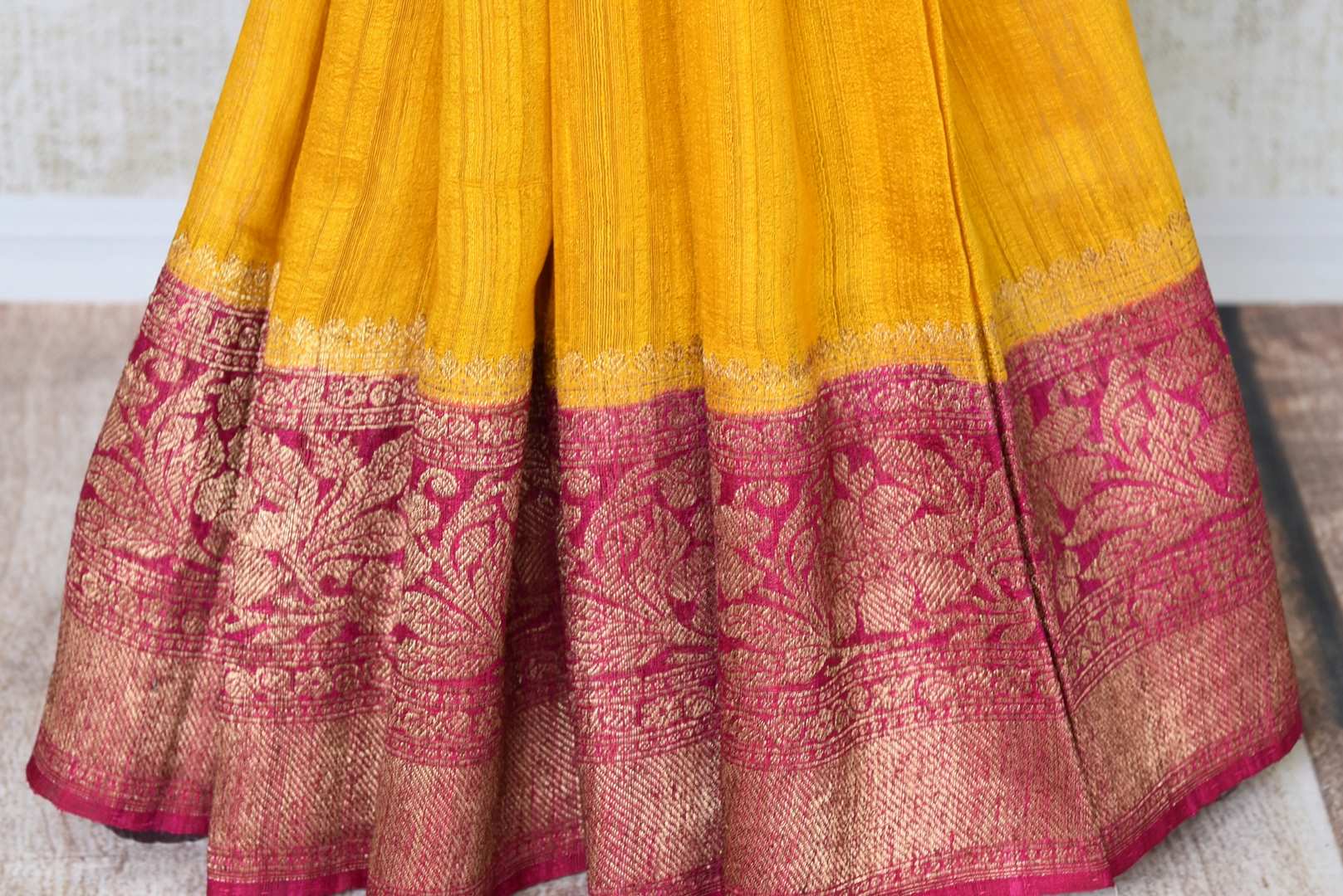 Shine bright like a sunshine in our vibrant yellow matka banarsi silk sari which is blended well with a pink zari border. Style this effervescent saree with a hot pink zari blouse to catch the fancy of folks around. Shop designer silk sarees, georgette sari, organza sari online or visit Pure Elegance store, USA.-pleats