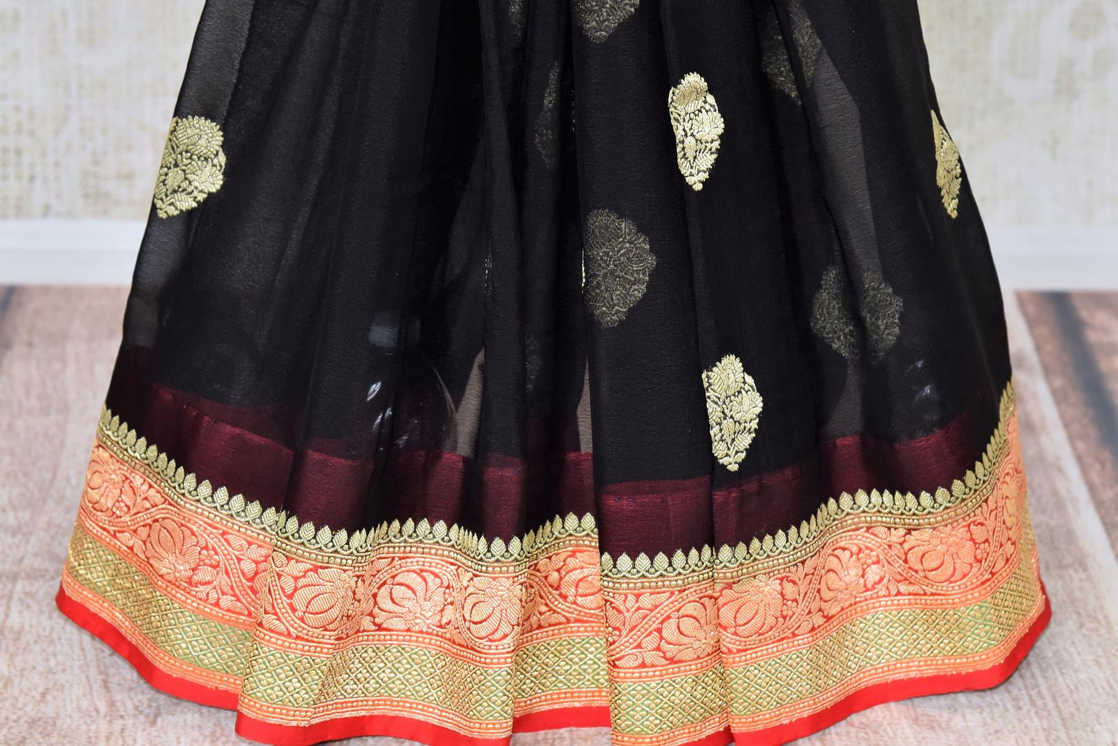 Buy stunning black georgette Benarasi saree online in USA with red floral zari border from Pure Elegance online store. Visit our exclusive Indian clothing store in USA and get floored by a range of exquisite pure handloom sarees, Banarasi sarees, silk sarees, Indian jewelry and much more to complete your ethnic look.-pleats