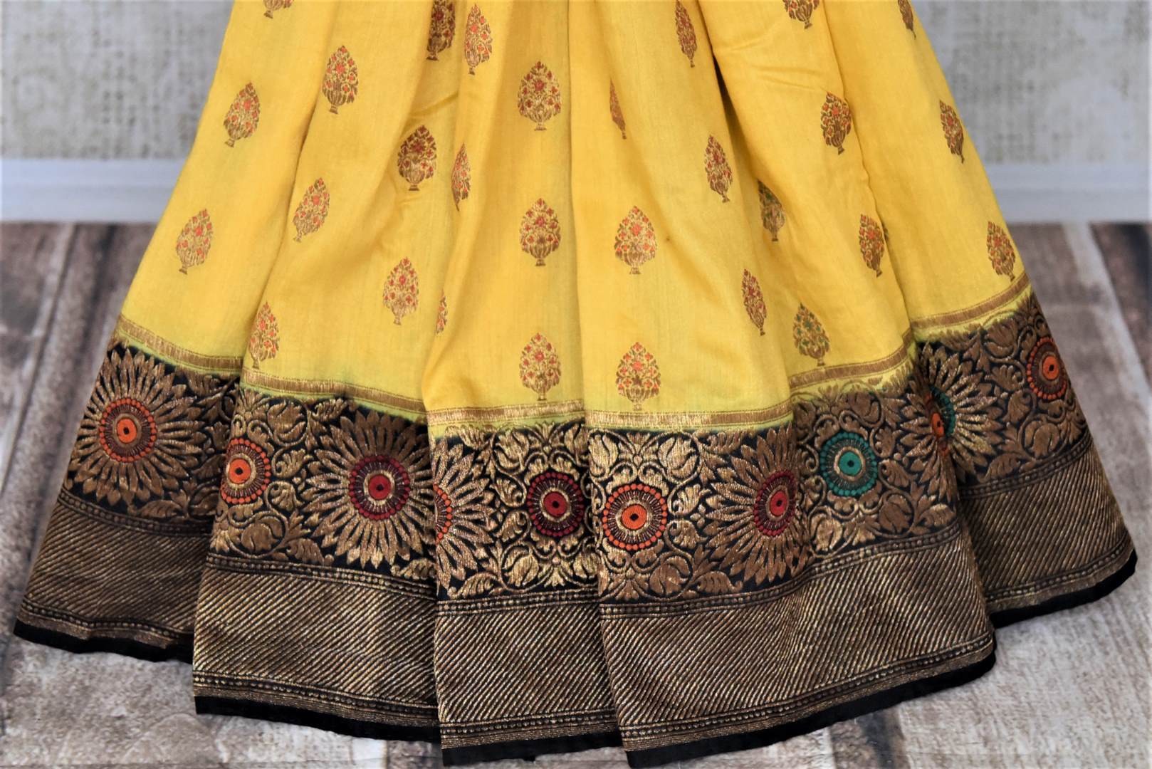 Shop stunning yellow muga Banarasi sari online in USA with black antique zari floral border. Keep your ethnic style updated with latest designer sarees, handloom sarees, pure silk sarees from Pure Elegance Indian fashion store in USA.-pleats